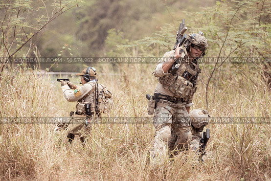 Soldiers in camouflage military uniforms carrying weapons, Reconnaissance missions in the tropical forest area with mission of helping those injured from being shot. Стоковое фото, агентство Ingram Publishing / Фотобанк Лори