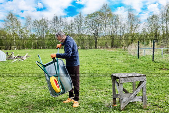 Solid polyurethane wheel is being tested as gardener lowers garden wheelbarrow to ground to evaluate smoothness and stability of newly installed wheel. Стоковое фото, фотограф Владимир Григорьев / Фотобанк Лори