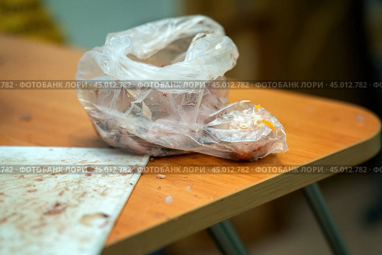 Solitary plastic bag containing fish entrails rests on a stark table, evoking themes of waste, consumption, and the overlooked remnants of everyday choices within a consumer society. Стоковое фото, фотограф Татьяна Степанищева / Фотобанк Лори