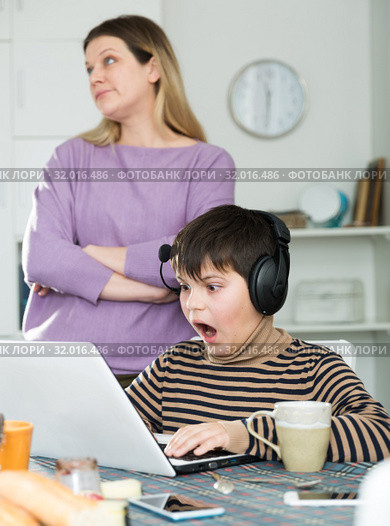 Son plaing video games at laptop, sad mom on background. Стоковое фото, фотограф Яков Филимонов / Фотобанк Лори