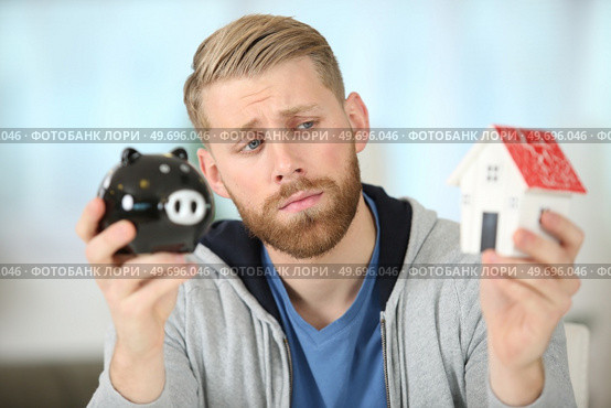 sorrowful man holding a piggybank and a model house. Стоковое фото, агентство Ingram Publishing / Фотобанк Лори