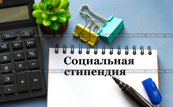 СОЦИАЛЬНАЯ СТИПЕНДИЯ - слова в белом блокноте на фоне калькулятора и зажимов. Стоковое фото, фотограф Жанна Гапанович / Фотобанк Лори