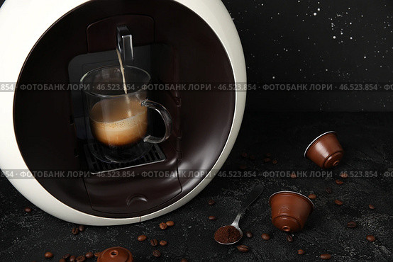 Современный кофейный аппарат с капсулами, капающим эспрессо, чашкой, кафе и зернами на черном гранж-столе. Стоковое фото, фотограф Pixel_shot / Фотобанк Лори