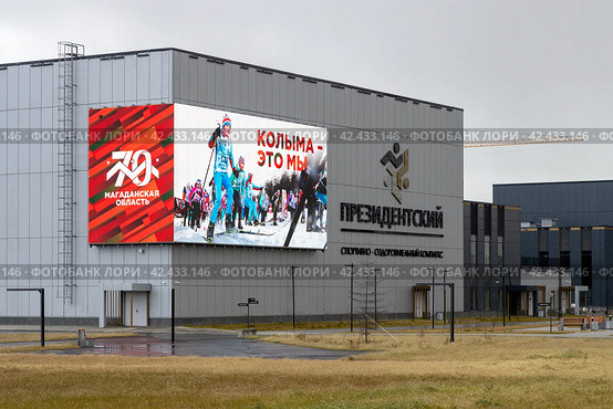 Спортивно-оздоровительный комплекс «Президентский», город Магадан, Магаданская область, Дальний Восток России. На здании спорткомплекса экран с фотографией лыжников и надписями «70 лет Магаданской области» и «Колыма – это мы». (2023 год). Редакционное фото, фотограф Андрей Степанов / Фотобанк Лори