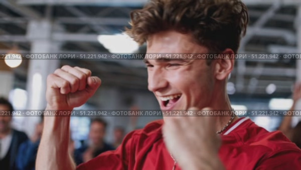 Sports enthusiast in red shirt jubilantly celebrating team win, raising fists with electric excitement amid roaring stadium crowd. Стоковое AI-видео, аниматор Юрий Поздников / Фотобанк Лори