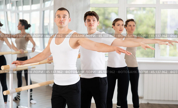 Sports young guy in black and white sportswear, participating 2nd position of ballet stance at barre with group in choreography studio. Стоковое фото, фотограф Яков Филимонов / Фотобанк Лори