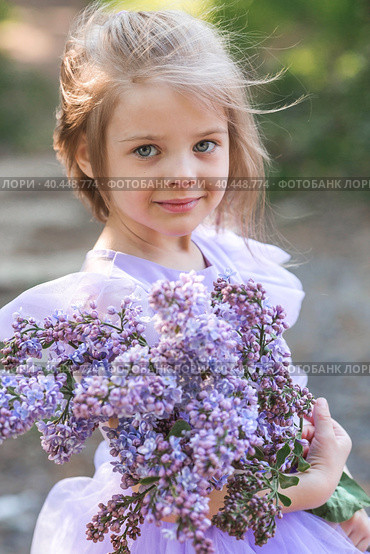 Spring flowering. Portrait of a beautiful little girl 4 years old in a lilac dress with a bouquet of lilac flowers in nature. Childhood. The baby poses and looks at the camera. Стоковое фото, фотограф Photojuli / Фотобанк Лори