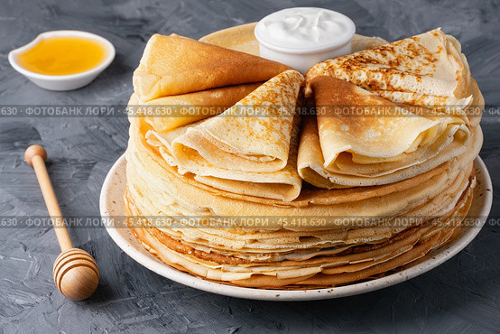 Stack of traditional russian pancakes blini with honey and sour creamon gray background. Стоковое фото, фотограф Наталия Попова / Фотобанк Лори