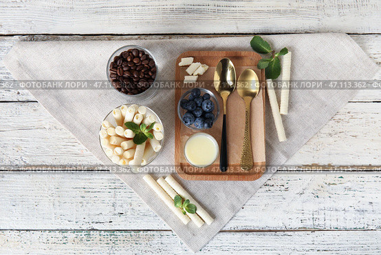 Стакан вкусных вафельных трубочек и доска со сгущенным молоком на белом деревянном фоне. Стоковое фото, фотограф Pixel_shot / Фотобанк Лори
