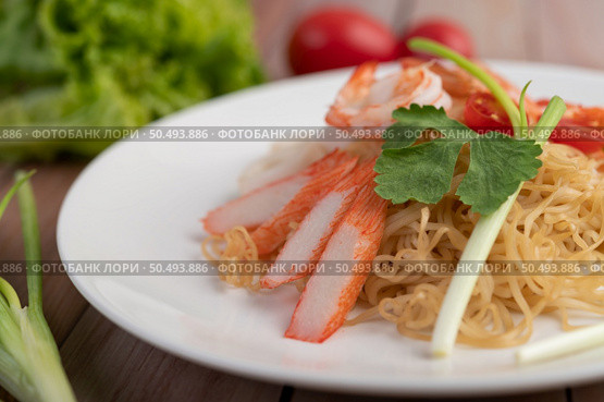 Stir-fried instant noodle with prawn and crab stick along with tomatoes and peppers in a white plate on a wooden floor. Стоковое фото, агентство Ingram Publishing / Фотобанк Лори
