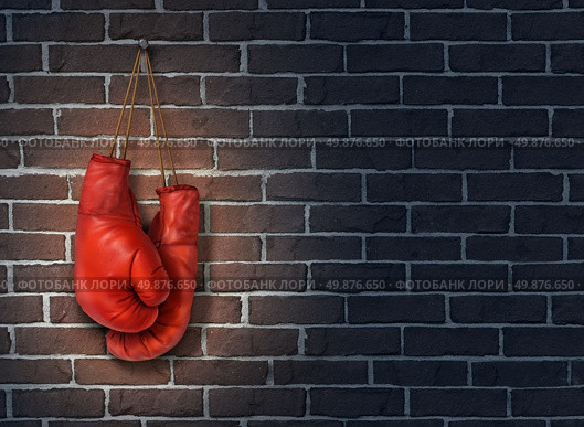 Stop competing and putting an end to business competition by hanging up a pair of red boxing gloves on a dark rustic old brick wall as a concept of stopping the fight to find the cure. Стоковое фото, агентство Ingram Publishing / Фотобанк Лори