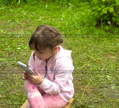 St.Petersburg,Russia-July 14,2025: A girl in colorful pink clothing looking at the smartphone on nature. Стоковое фото, фотограф Андрей Митин / Фотобанк Лори