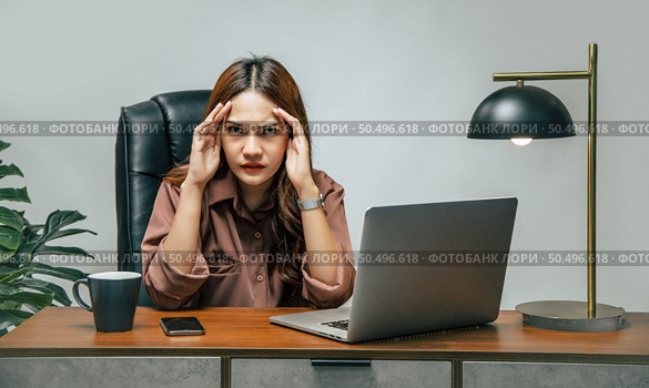 Stressed young working woman sitting at her desk, she works from home on laptop computer and smartphone during self-isolation and quarantine covid-19 coronavirus outbreak. Стоковое фото, агентство Ingram Publishing / Фотобанк Лори