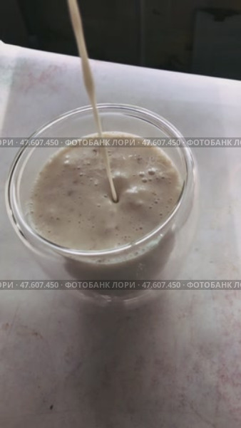 Струйка густого молочно-бананового смузи стекает в прозрачный стакан. Стоковое видео, видеограф Ярославский Максим / Фотобанк Лори