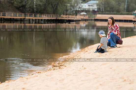 Summer lifestyle. A cute little boy and his mom are having fun playing with sand on the beach by the water. The concept of family entertainment and leisure. Стоковое фото, фотограф Photojuli / Фотобанк Лори