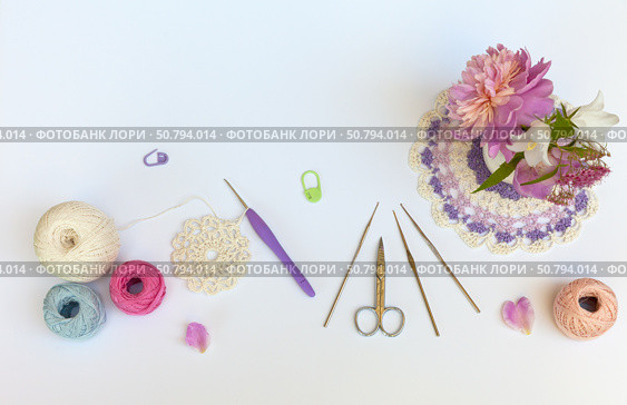 Summer needlework. Crochet openwork napkin. Bouquet of flowers, set of crochet hooks, skeins of cotton yarn, scissors on a white background. DIY concept. Copy space, flat lay, close-up, top view. Стоковое фото, фотограф Виктория Катьянова / Фотобанк Лори