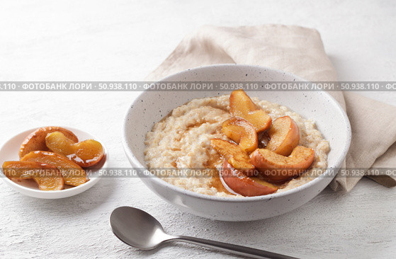 Sweet oatmeal porridge with baked apple slices, cinnamon and caramel sauce in a gray bowl on a light background, top view. Delicious homemade food. Стоковое фото, фотограф Ольга Лепёшкина / Фотобанк Лори