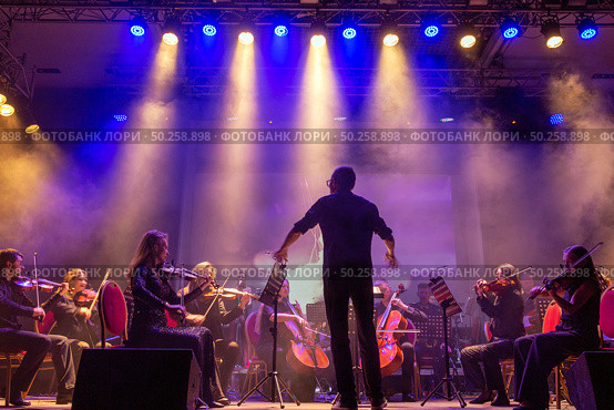 Symphony orchestra performing on stage under bright spotlights and stage lights (2024 год). Редакционное фото, фотограф Евгений Ткачёв / Фотобанк Лори