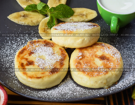Syrniki or cheese pancakes with cream sauce and bananas on a plate on wooden table close up. Стоковое фото, фотограф Татьяна Терехина / Фотобанк Лори