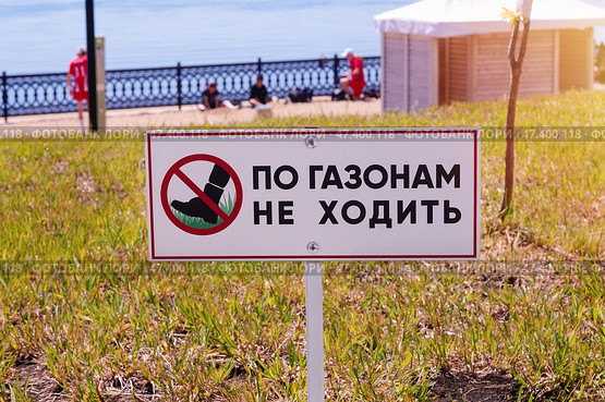 Табличка По газонам не ходить с изображением ноги в красном перечеркнутом круге на фоне набережной и отдыхающих спортсменов (2024 год). Стоковое фото, фотограф Евгения Золкина / Фотобанк Лори