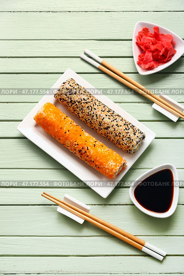 Тарелка с вкусными роллами суши, имбирем, палочками и соевым соусом на деревянном фоне. Стоковое фото, фотограф Pixel_shot / Фотобанк Лори