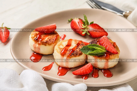Тарелка с вкусными сырниками, покрытыми соусом и ягодами на белом деревянном столе. Стоковое фото, фотограф Pixel_shot / Фотобанк Лори