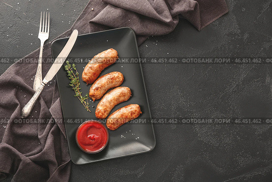 Тарелка с вкусными жареными колбасками и соусом на темном фоне. Стоковое фото, фотограф Pixel_shot / Фотобанк Лори
