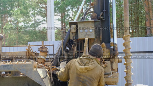 Team of workers with drilling rig on car are drilling artesian well for water in ground. Insertion of metal casing pipe into ground, installation of individual drinking supply, June 28, 2022, Russia, Palaces. Редакционное видео, видеограф Ольга Симонова / Фотобанк Лори