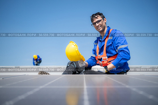 Technician repairing solar panels take off his hat and rest in the scorching sun on a factory roof covered with solar panels to receive solar energy. Стоковое фото, агентство Ingram Publishing / Фотобанк Лори