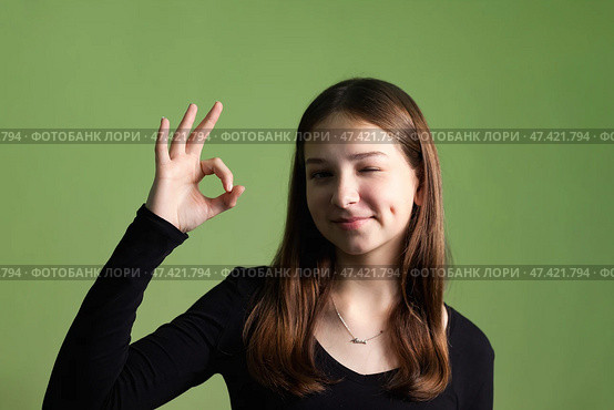 Teen Girl Expresses Confidence With a Playful Gesture Against a Green Background in a Studio Setting. Стоковое фото, фотограф Aleksandr Golubev / Фотобанк Лори