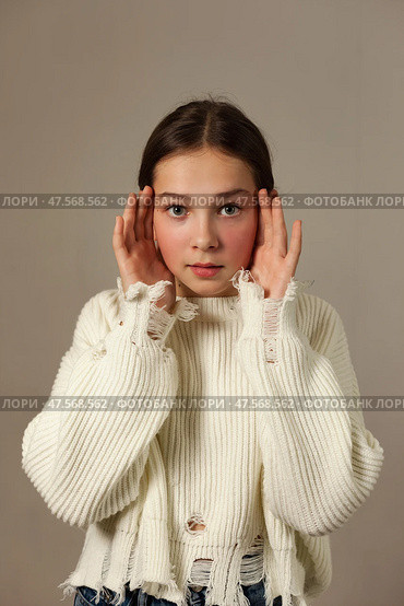 Teen Girl Expressing Curiosity While Posing in a Cozy Sweater Against a Neutral Backdrop. Стоковое фото, фотограф Aleksandr Golubev / Фотобанк Лори