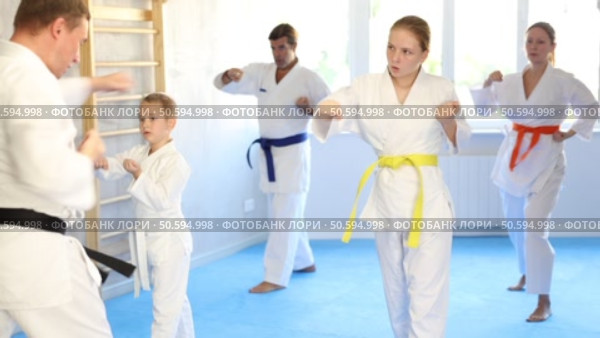 Teen girl with family repeat movements and learn fighting techniques during martial arts lesson. Стоковое видео, видеограф Яков Филимонов / Фотобанк Лори