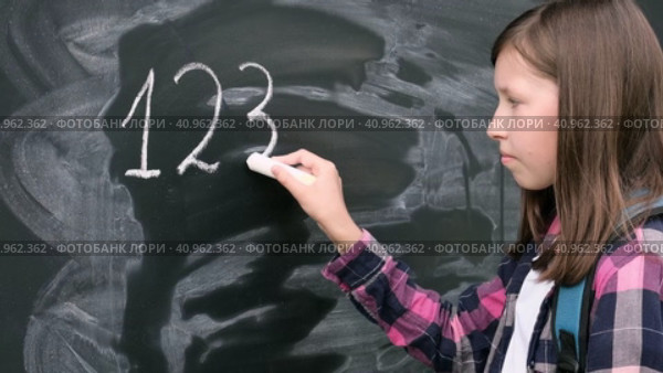 Teenage student girl in shirt with blue backpack writing with chalk numbers and letters on black chalkboard background. Education, back to school and people concept. Joyful Teen girl near blackboard. Стоковое видео, видеограф Марина Демидюк / Фотобанк Лори