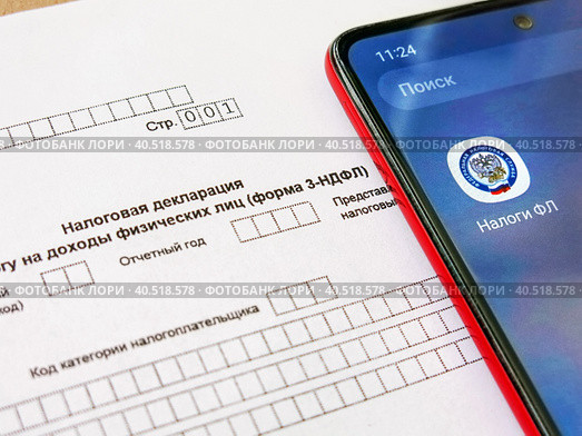 Телефон с электронным приложением налоговой службы "Налоги ФЛ" лежит на бланке налоговой декларации 3-НДФЛ. Оформление социального и имущественного вычета через интернет (2023 год). Редакционное фото, фотограф Татьяна Т / Фотобанк Лори