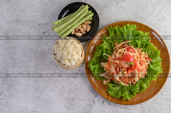 Thai papaya salad on salad in a wooden plate with Sticky rice, Yardlong beans, and garlic. Top view. Стоковое фото, агентство Ingram Publishing / Фотобанк Лори