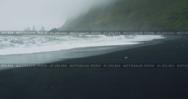 The black sand beach of Reynisfjara with waves hitting the shore on foggy rainy stormy day Vik, Icel. Стоковое видео, видеограф Igor Tichonow / Фотобанк Лори