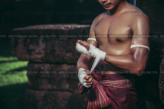 The boxer sat on the stone, tied the tape around his hand, preparing to fight. Стоковое фото, агентство Ingram Publishing / Фотобанк Лори