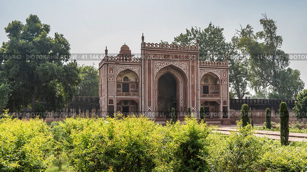 The building in the tomb of Itmad-Ud-Daulah complex is built of red sandstone, decorated with white ornaments. Arches and domes are visible. There is a wall around the perimeter of the garden. Agra (2022 год). Стоковое фото, фотограф Вера Ивановна Кубарева / Фотобанк Лори