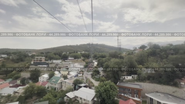 The cable car cabin moves towards Kok-Tobe mountain above the low-rise buildings of the city. Kazakhstan. Alama-ata. 24.08.2024. Редакционное видео, видеограф Ярославский Максим / Фотобанк Лори