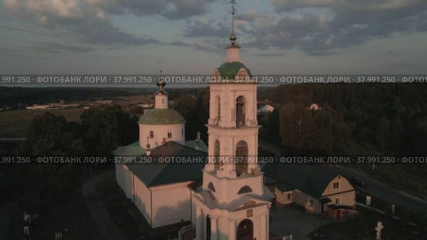 The camera flies over the evening Orthodox church with a bell tower. The village of Rakhmanovo, Moscow region, Pavloposadsky district. Aerial photography. Стоковое видео, видеограф Ярославский Максим / Фотобанк Лори