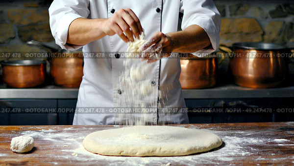 The cook prepares the dough for the product in the form of a pizza. The chef makes pizza for the customers. The pizza maker prepares pizza dough. Стоковое AI-изображение, AI-художник Антон Слабоспицкий / Фотобанк Лори