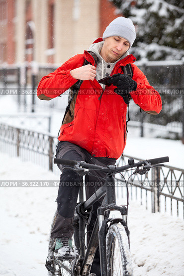The delivery man puts his smartphone in his jacket pocket while sitting on bicycle at winter season. Стоковое фото, фотограф Кекяляйнен Андрей / Фотобанк Лори