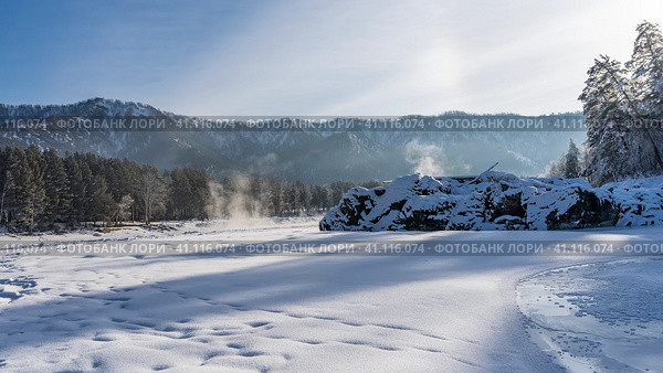 The frozen river is covered with pure snow. Steam rises above the polynya. Picturesque boulders and forest along the banks. Mountains against the blue sky. Altai. Katun. Стоковое фото, фотограф Вера Ивановна Кубарева / Фотобанк Лори