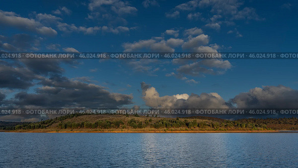 The golden hour of the evening. A calm lake with hilly shores. Green vegetation on the red soil of the hills. The clouds in the blue sky are highlighted. Madagascar. Mantasoa lake. Стоковое фото, фотограф Вера Ивановна Кубарева / Фотобанк Лори