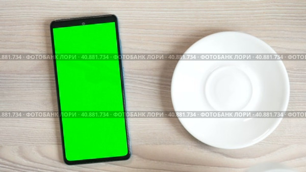 The green screen of a smartphone or chroma key on the table, a cup of coffee. Coffee break, click the touch screen. Close up Mock up. Стоковое видео, видеограф Глущенко Елена / Фотобанк Лори
