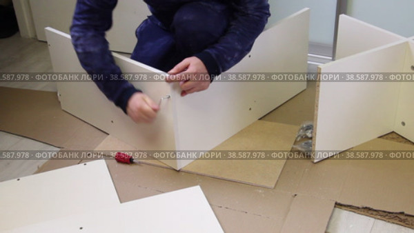The man connects the side panel and the cover with a Euro screw. Wooden modular rack. Assembling a modular rack. Overall plan. Стоковое видео, видеограф Vadzim Yakubovich / Фотобанк Лори