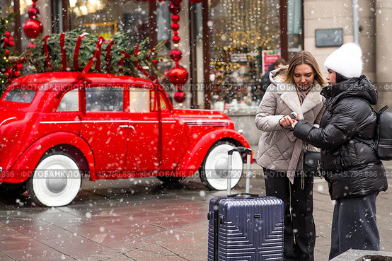 The new year is 2025. Tourists girls with a suitcase in the center of Moscow. Tourism in Russia for the New Year holidays. New Year decorations in Moscow. Christmas holidays. Russia, Moscow, December 2024. Редакционное фото, фотограф Photojuli / Фотобанк Лори