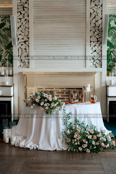 The presidium of the newlyweds in the banquet hall of the restaurant is decorated with candles and green plants, wisteria hangs from the ceiling. Стоковое фото, агентство Ingram Publishing / Фотобанк Лори