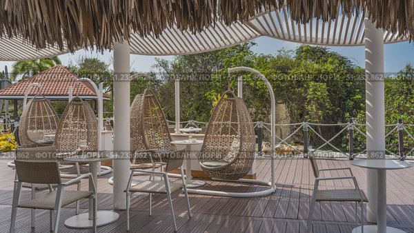 The recreation area at the resort. Wicker swings, tables, chairs on the outdoor terrace. Rope railings, latticed and thatched awnings. Green tropical vegetation. Cuba. Varadero. Стоковое фото, фотограф Вера Ивановна Кубарева / Фотобанк Лори