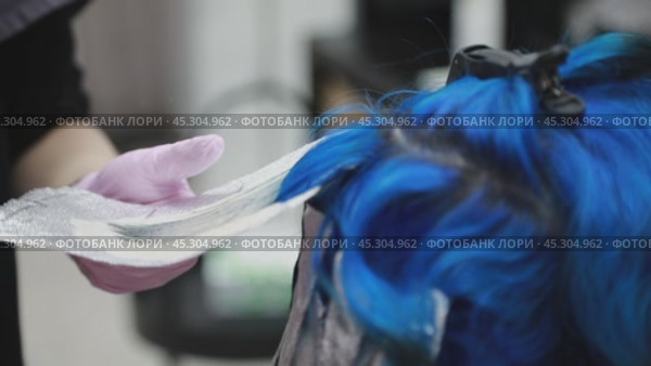 The stylist applies blue dye to a strand and carefully wraps it in foil for the best results. Стоковое AI-видео, аниматор Юрий Поздников / Фотобанк Лори